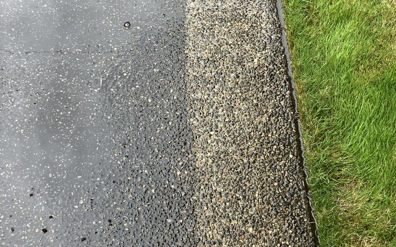 A driveway mid-wash, showing a sharp line between the freshly cleaned concrete and the dirty, darkened section still to be done.